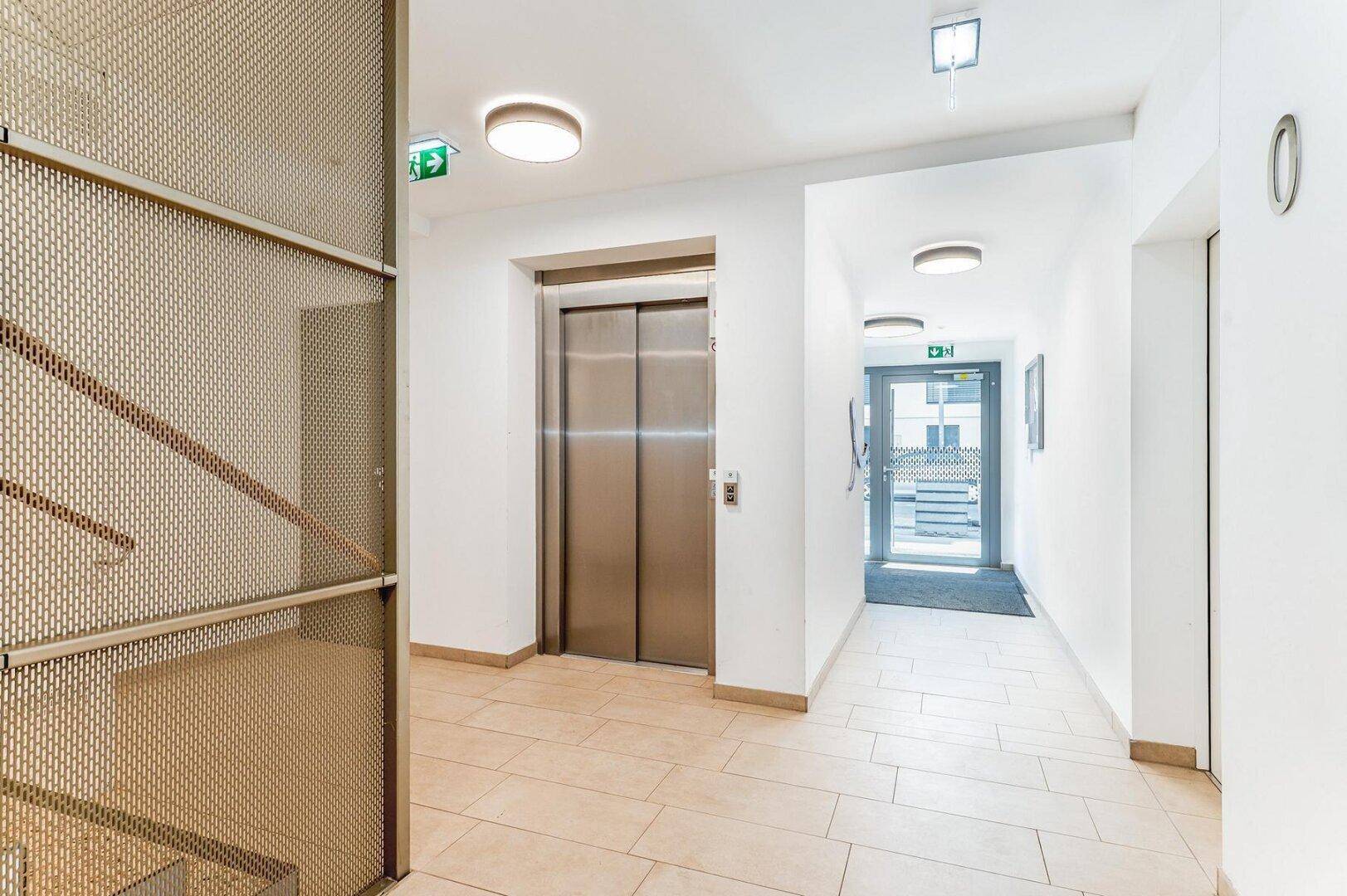 Moderner Eingangsbereich mit Aufzug und Zugang zum Treppenhaus, hell und einladend gestaltet.