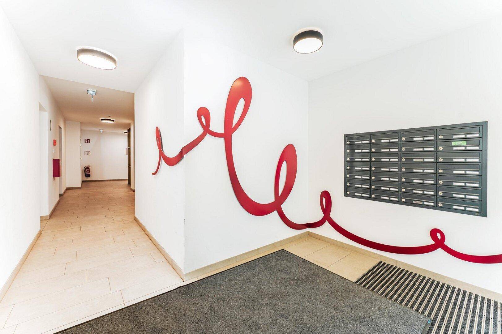 Eingangsbereich mit Briefkästen und dekorativer roter Wandgestaltung, modern und funktional.