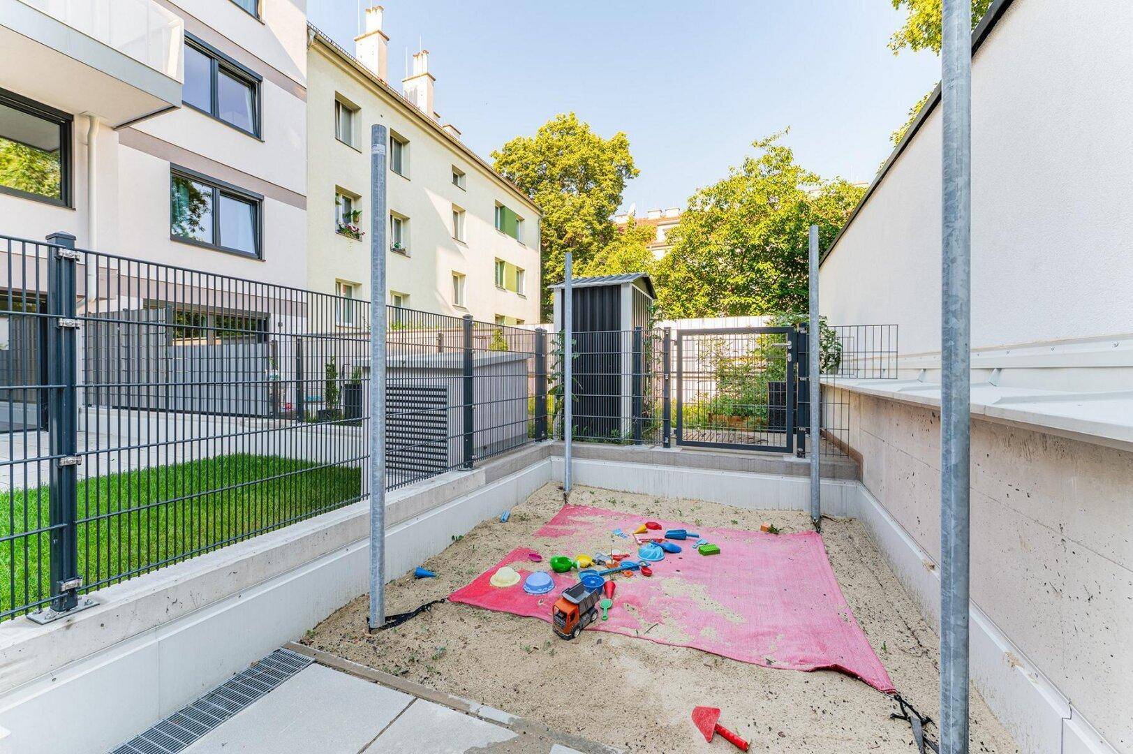 Kleiner Sandkasten mit Spielzeug im gemeinschaftlichen Außenbereich, ideal für Kinder.