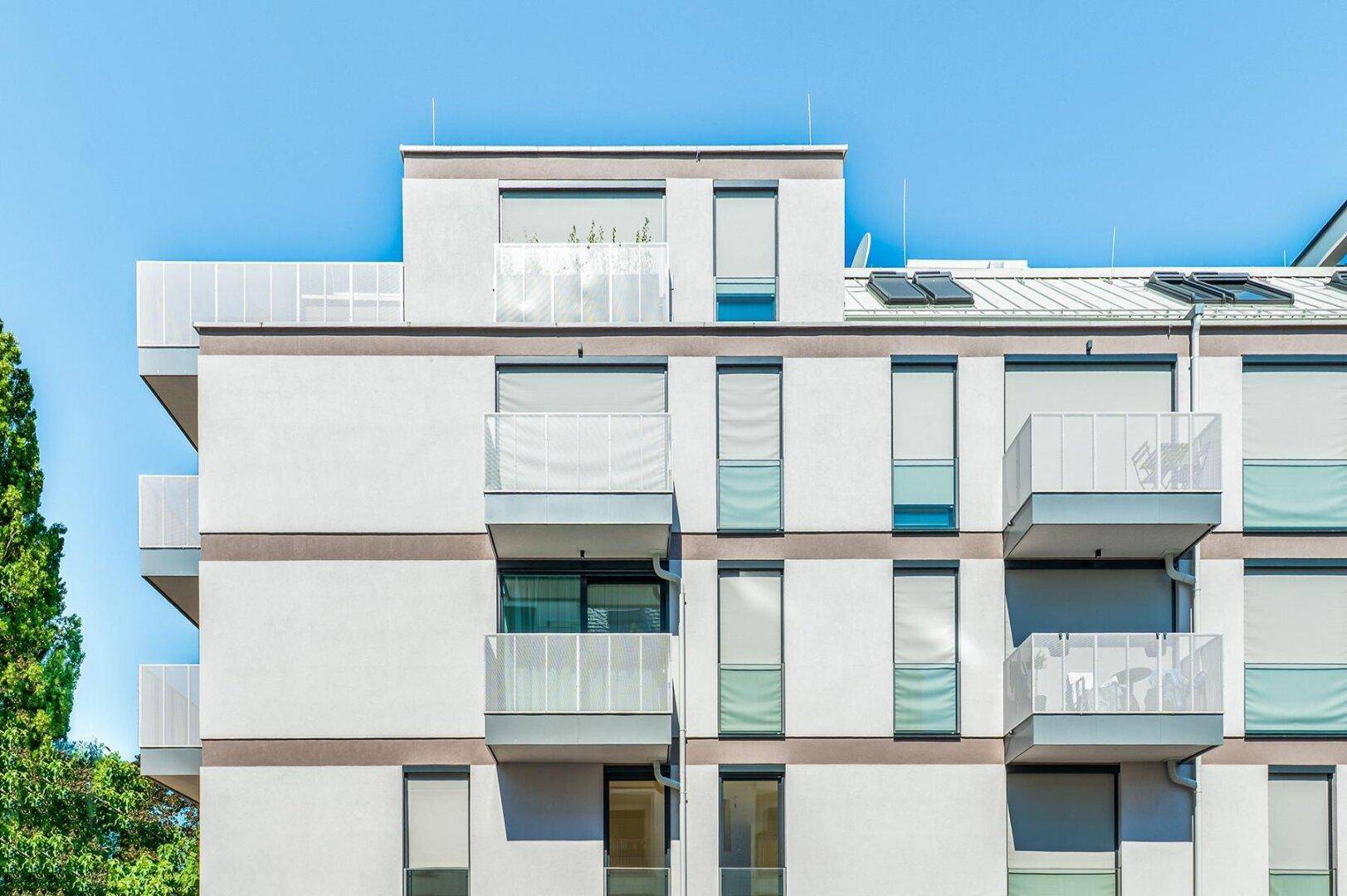 Fassade eines Neubaus mit Balkonen und Sonnenschutzrollos, bietet modernen Wohnkomfort.