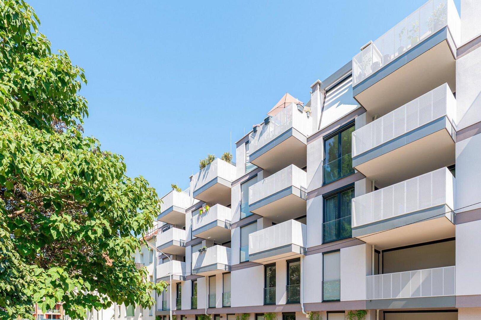 Moderne Wohnanlage mit zahlreichen Balkonen und großen Fenstern unter blauem Himmel.