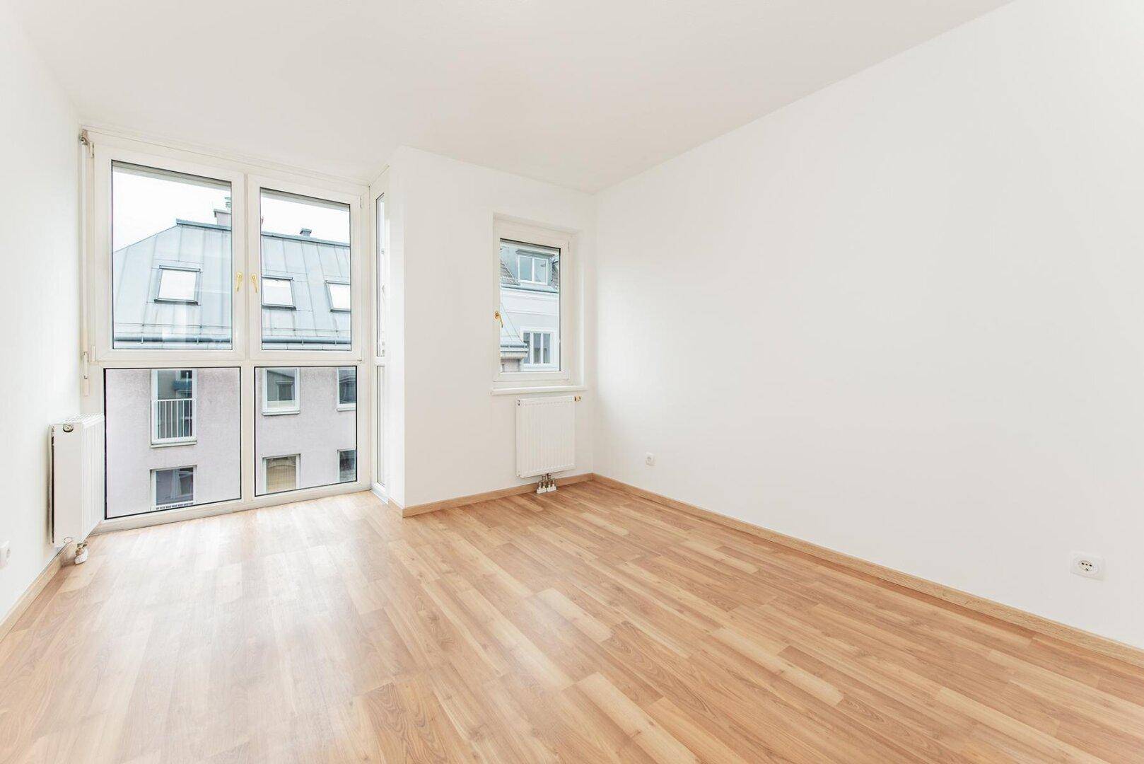 Geräumiges, helles Zimmer mit Laminatboden und großen Fenstern, die den Raum erhellen.