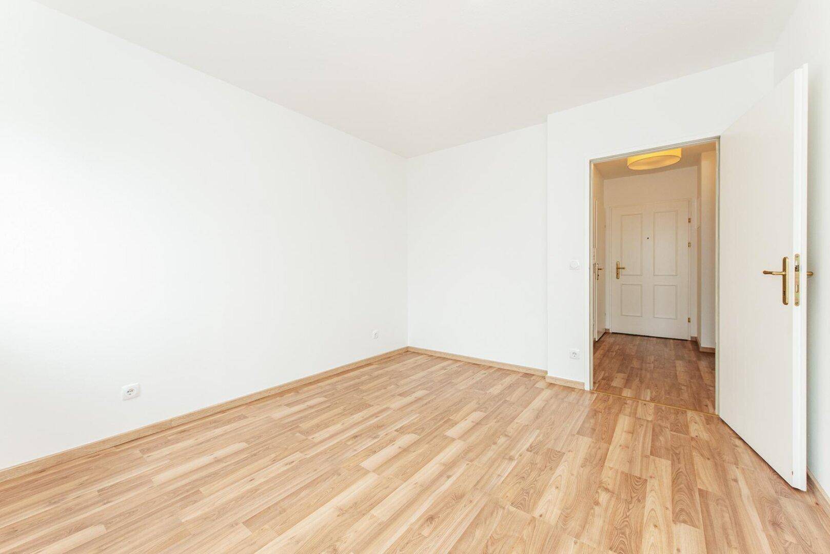 Leeres Zimmer mit Laminatboden und weiß gestrichenen Wänden, bereit für neue Einrichtung.