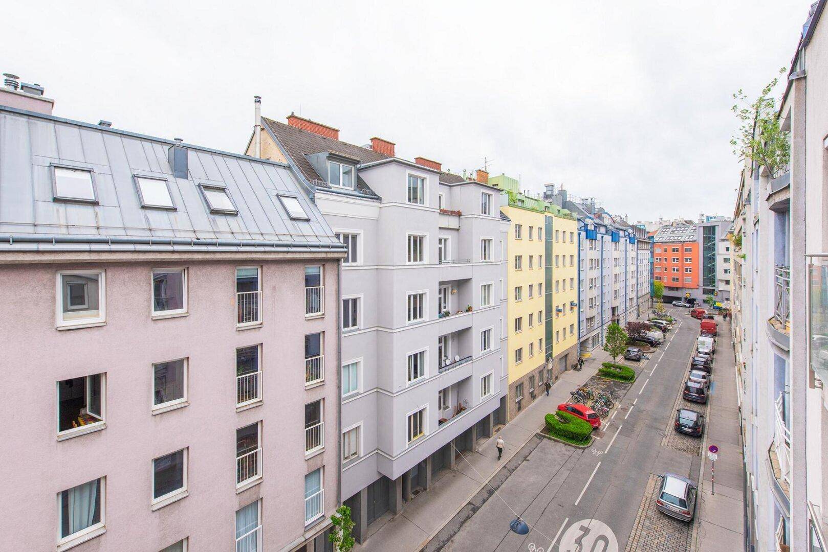 Blick auf eine belebte Stadtstraße mit mehrstöckigen Wohngebäuden und parkenden Autos.
