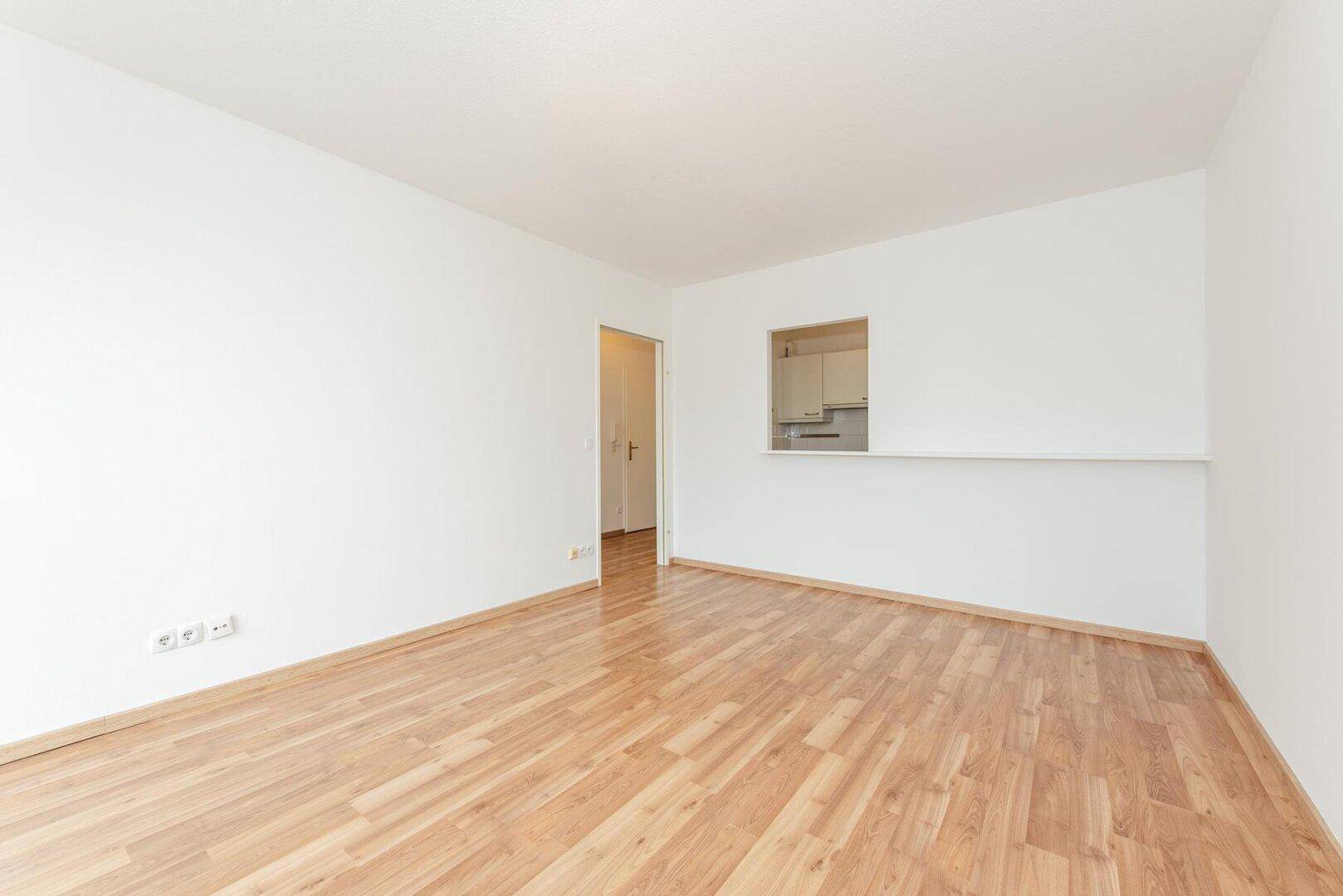 Heller Wohnbereich mit Laminatboden und Durchreiche zur Küche, ideal für offenes Wohnen.
