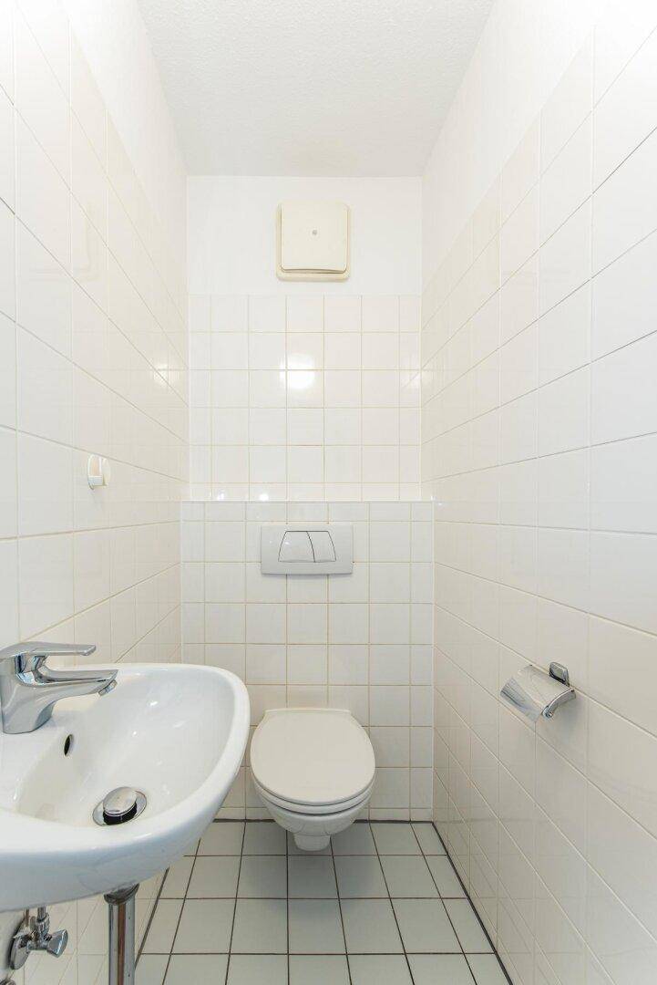 Separates WC mit wandhängender Toilette und kleinem Waschbecken, komplett gefliest.