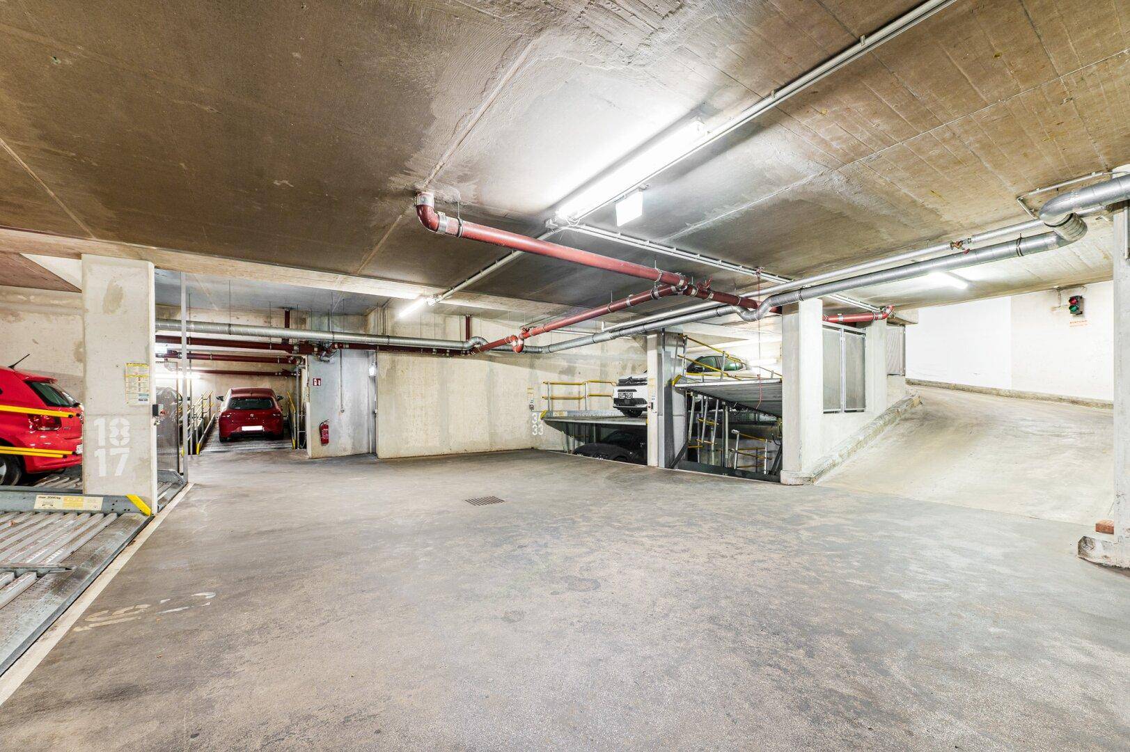 Weitläufige Tiefgarage mit Betonboden und mehreren Parkebenen, gut beleuchtet.