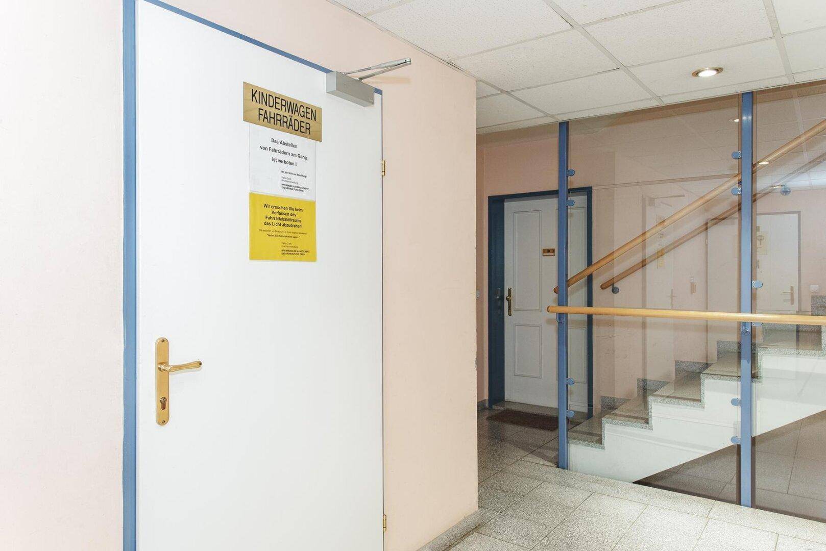 Eingangsbereich mit Hinweisschildern für Kinderwagen und Fahrräder, neben dem Treppenhaus.