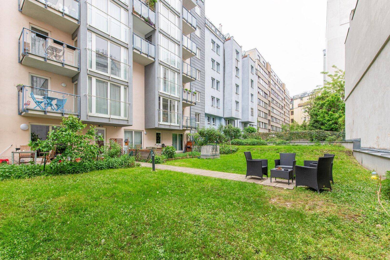 Gepflegter Gemeinschaftsgarten mit Rasenfläche und Sitzgelegenheiten, umgeben von Wohngebäuden.