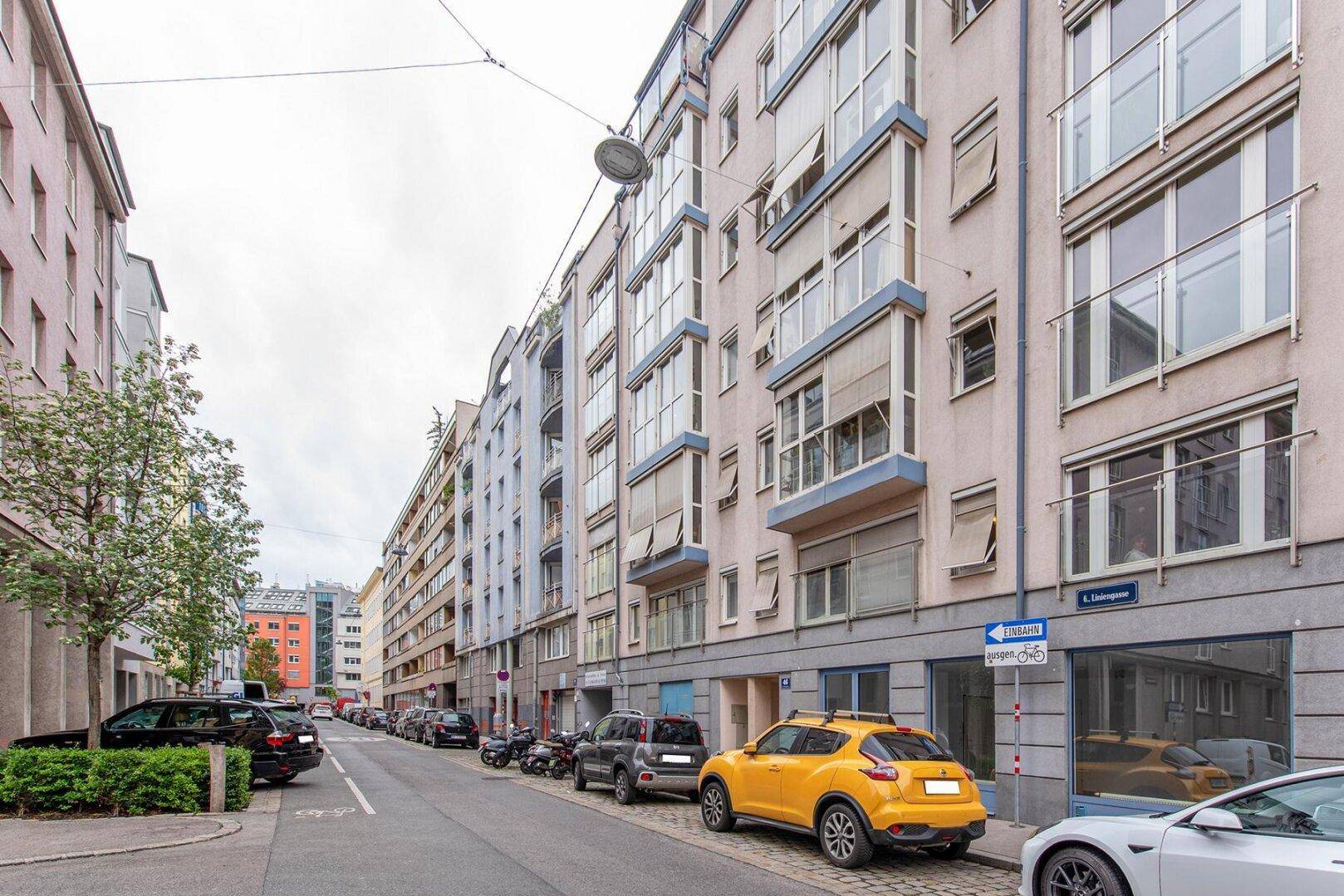 Blick auf eine städtische Straße mit parkenden Autos und modernen Wohngebäuden.