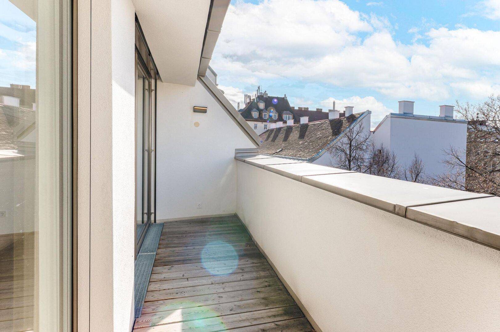 Geräumiger Balkon mit Holzdielen und weitem Blick über die städtische Dachlandschaft.