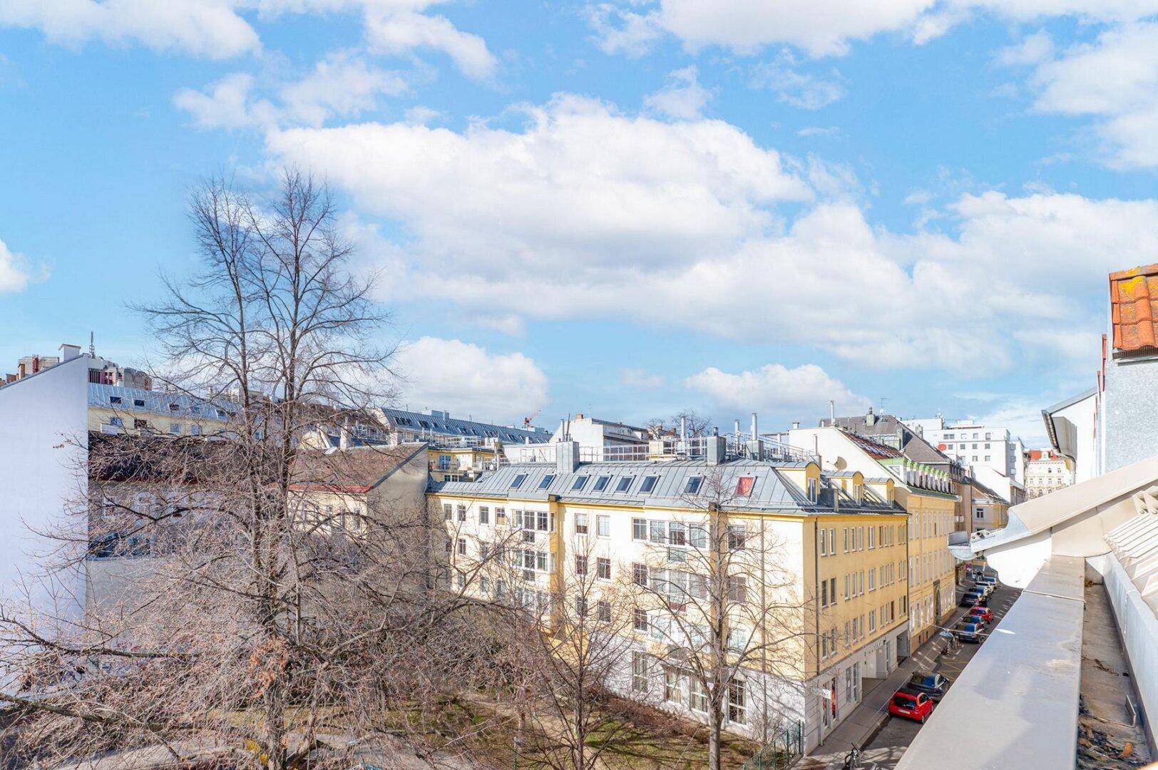 Weitläufiger Blick über die Stadt mit historischen Gebäuden und Bäumen unter blauem Himmel.