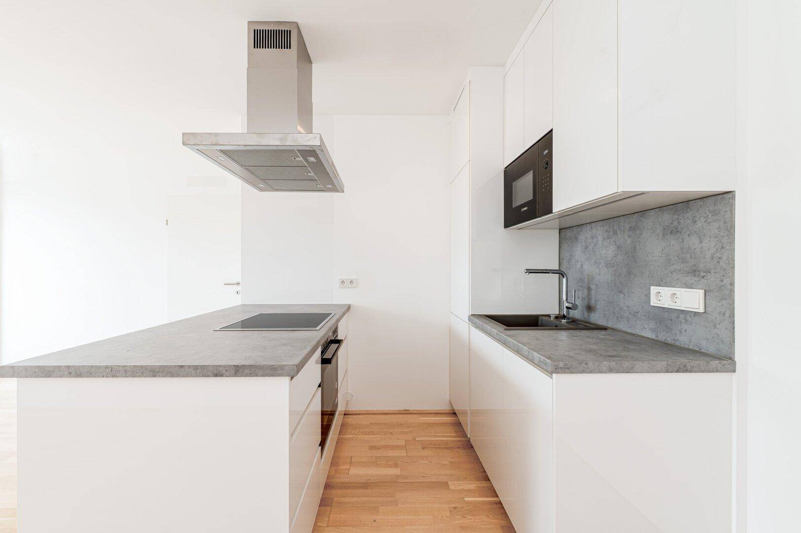 Moderne Einbauküche mit weißen Schränken, grauen Arbeitsplatten und integriertem Kochfeld.
