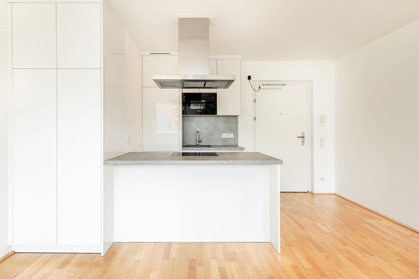 Moderne Küche mit weißen Hochglanzfronten, grauer Arbeitsplatte und praktischer Kücheninsel.