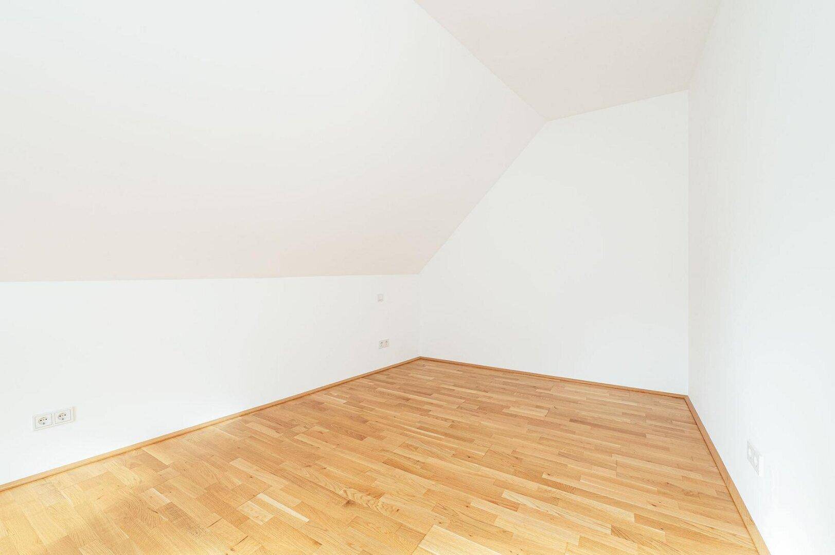 Geräumiges Zimmer mit Parkettboden, weißen Wänden und charakteristischer Dachschräge.