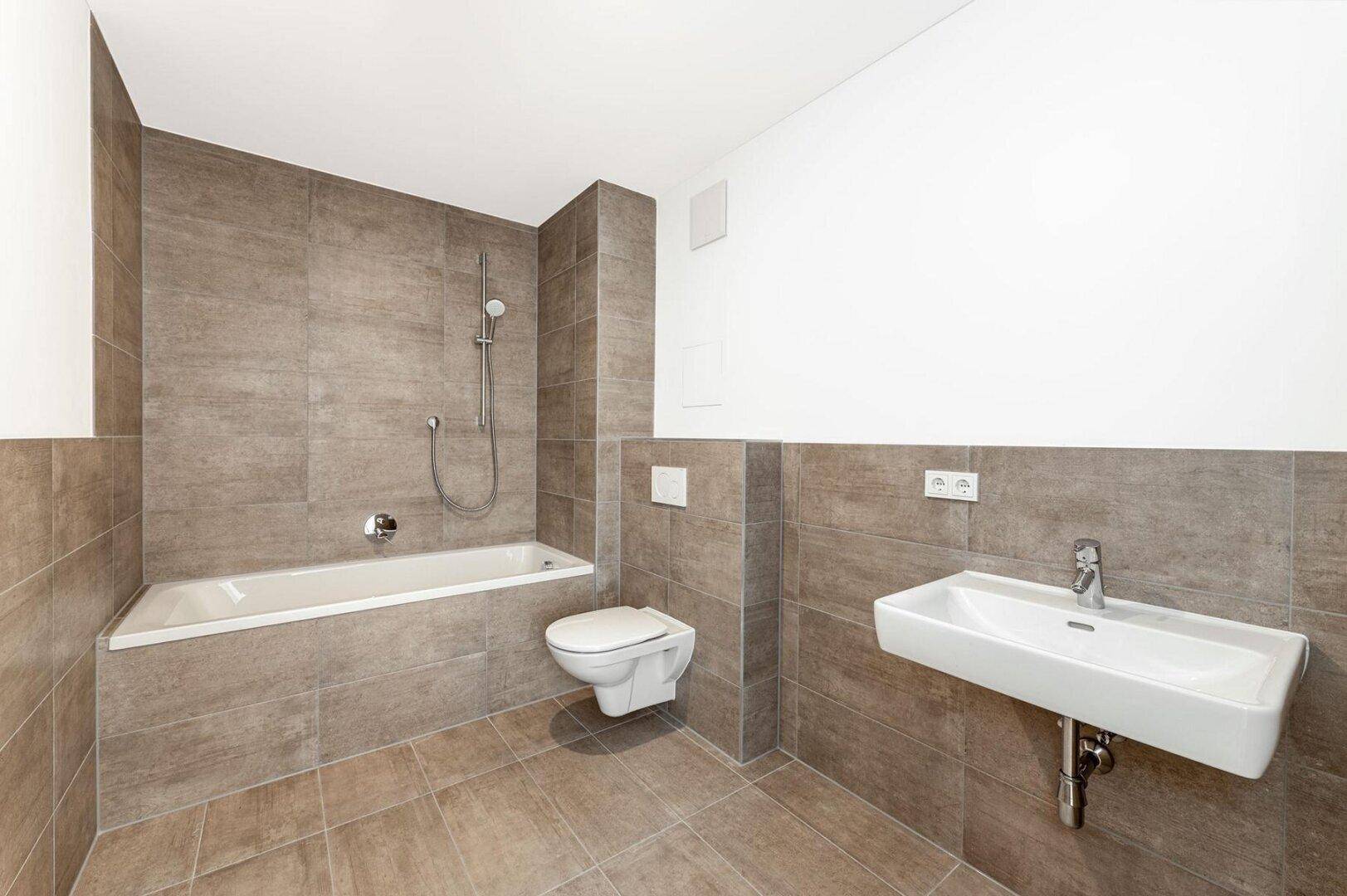 Modernes Badezimmer mit braunen Fliesen, Badewanne mit Duschfunktion und wandhängendem WC.