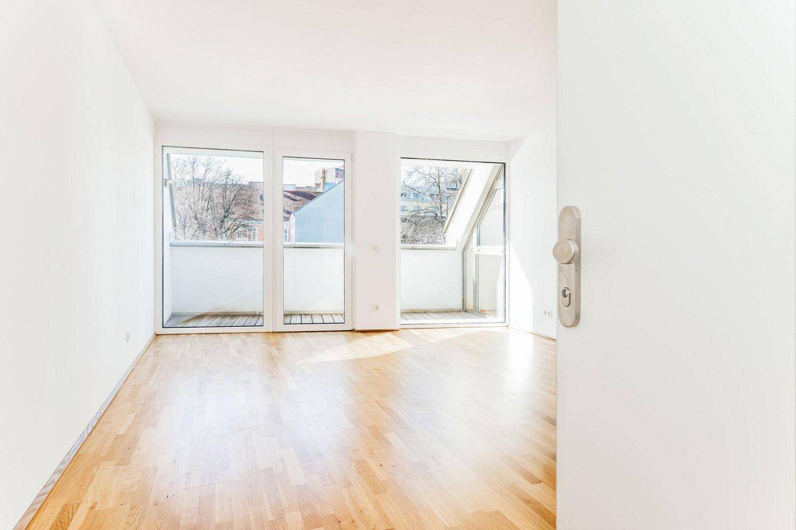Lichtdurchflutetes Wohnzimmer mit Parkettboden und großen Fenstern, die zu Balkonen führen.