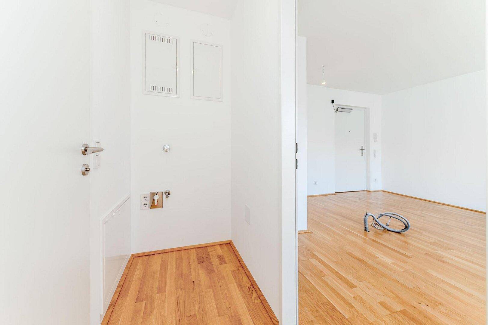 Praktischer Hauswirtschaftsraum mit Holzboden und Anschlüssen für Waschmaschine und Trockner.