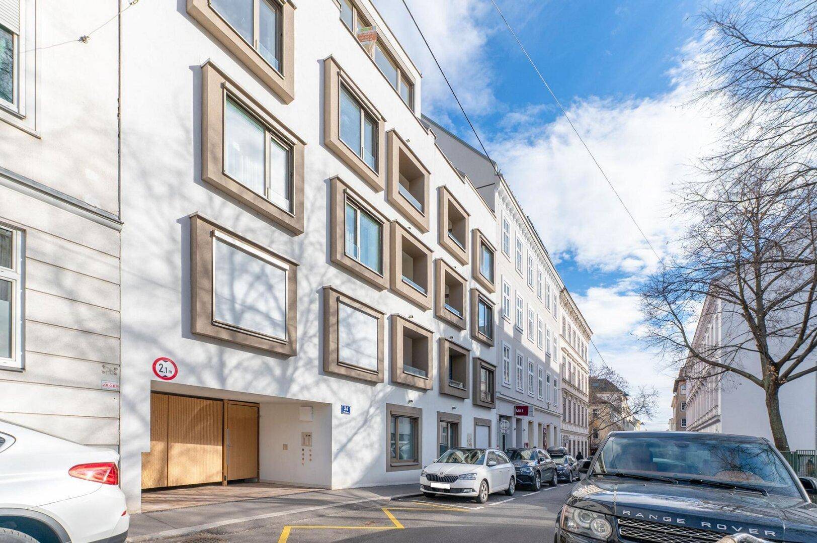 Moderne Gebäudefassade mit markanten Fenstern und Garageneinfahrt an einer städtischen Straße.