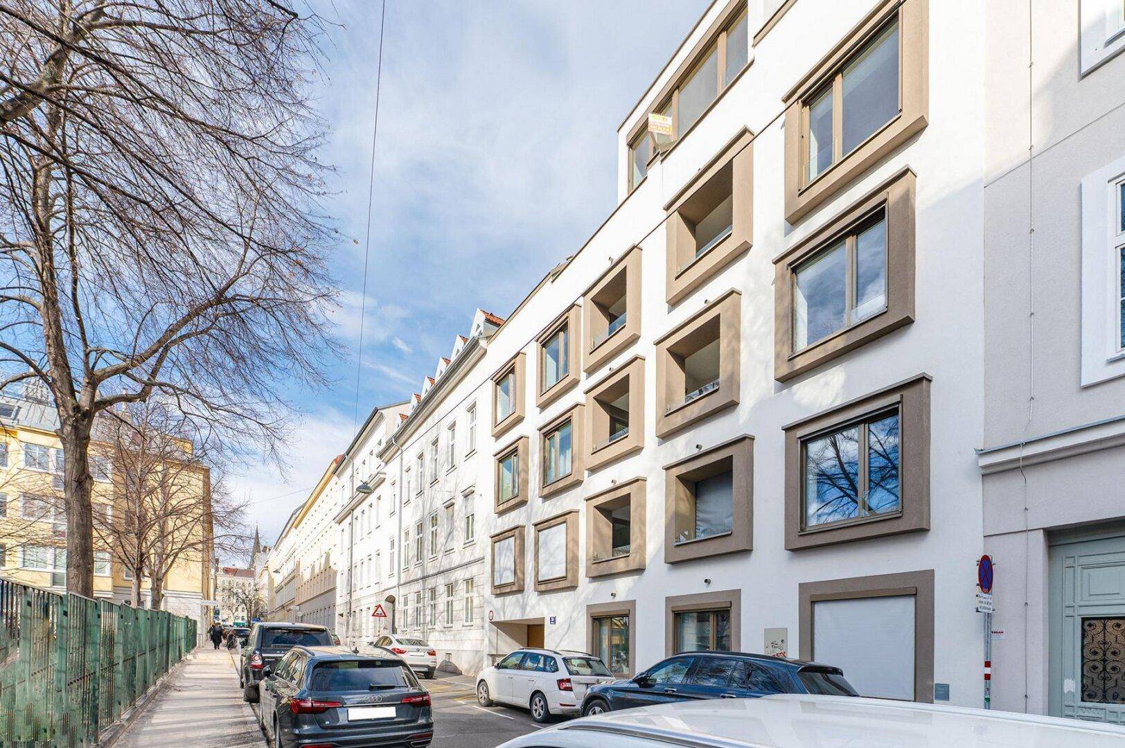 Ansicht der modernen Wohngebäude entlang einer Straße mit parkenden Autos und Bäumen.