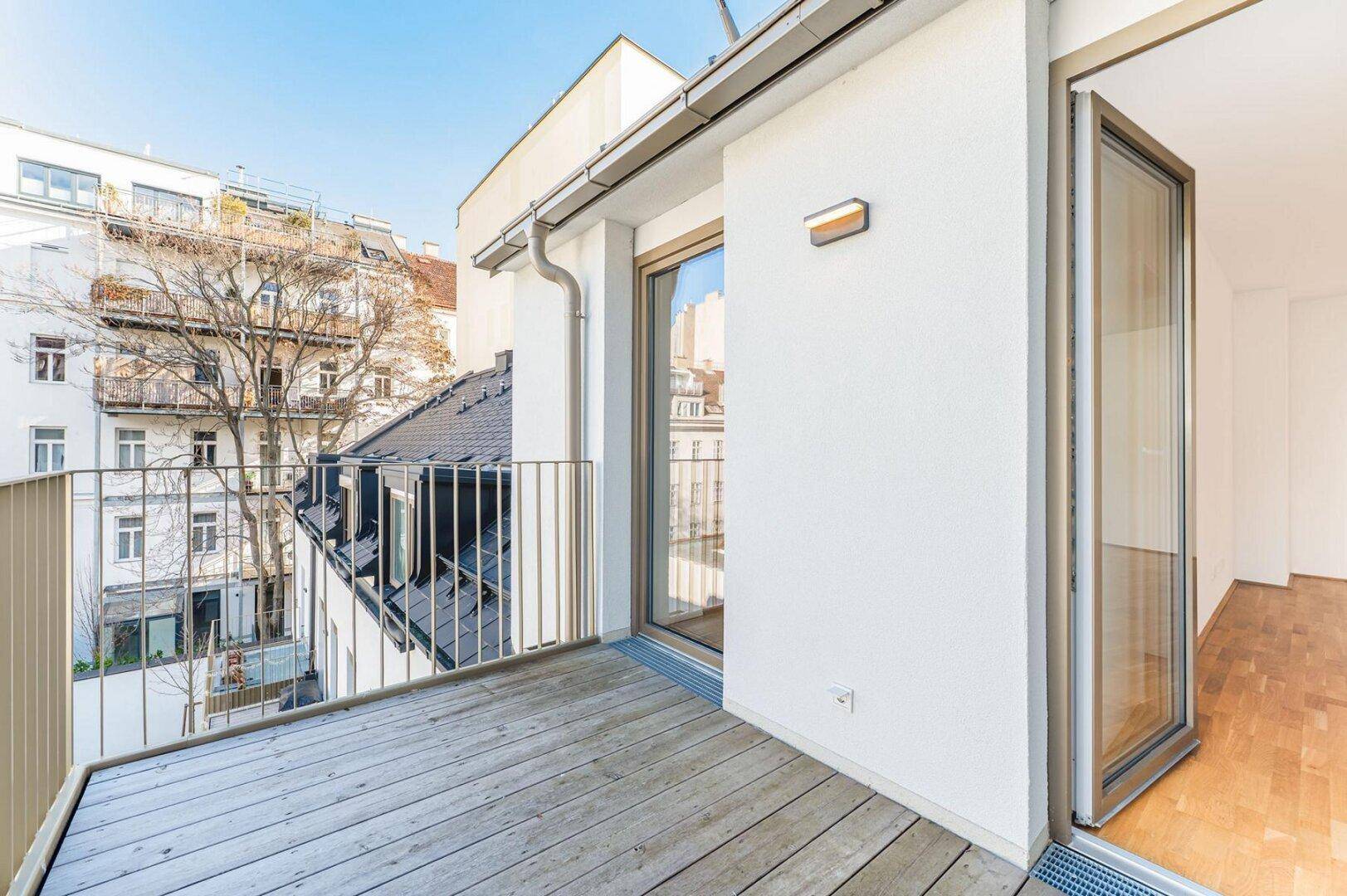 Heller Balkon mit Holzboden und Zugang zu einem lichtdurchfluteten Innenraum.