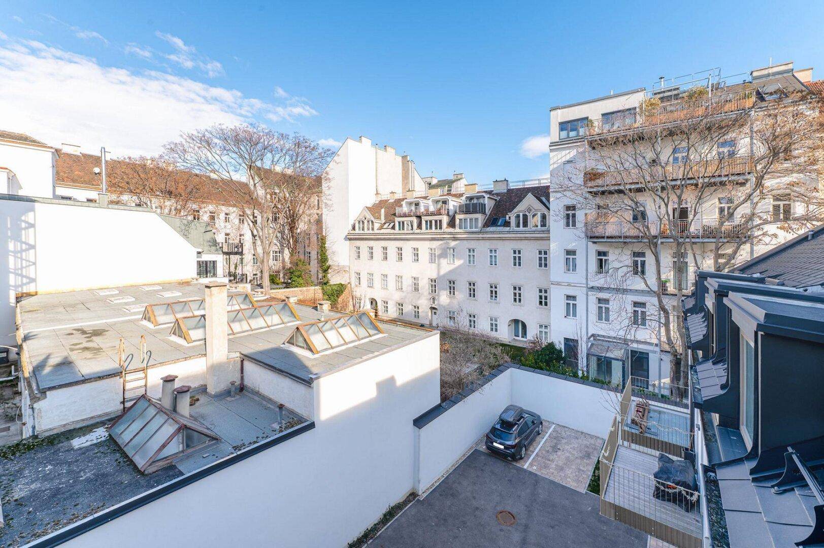 Blick von oben auf die Innenhöfe und Dächer der umliegenden Gebäude mit Parkplatz.
