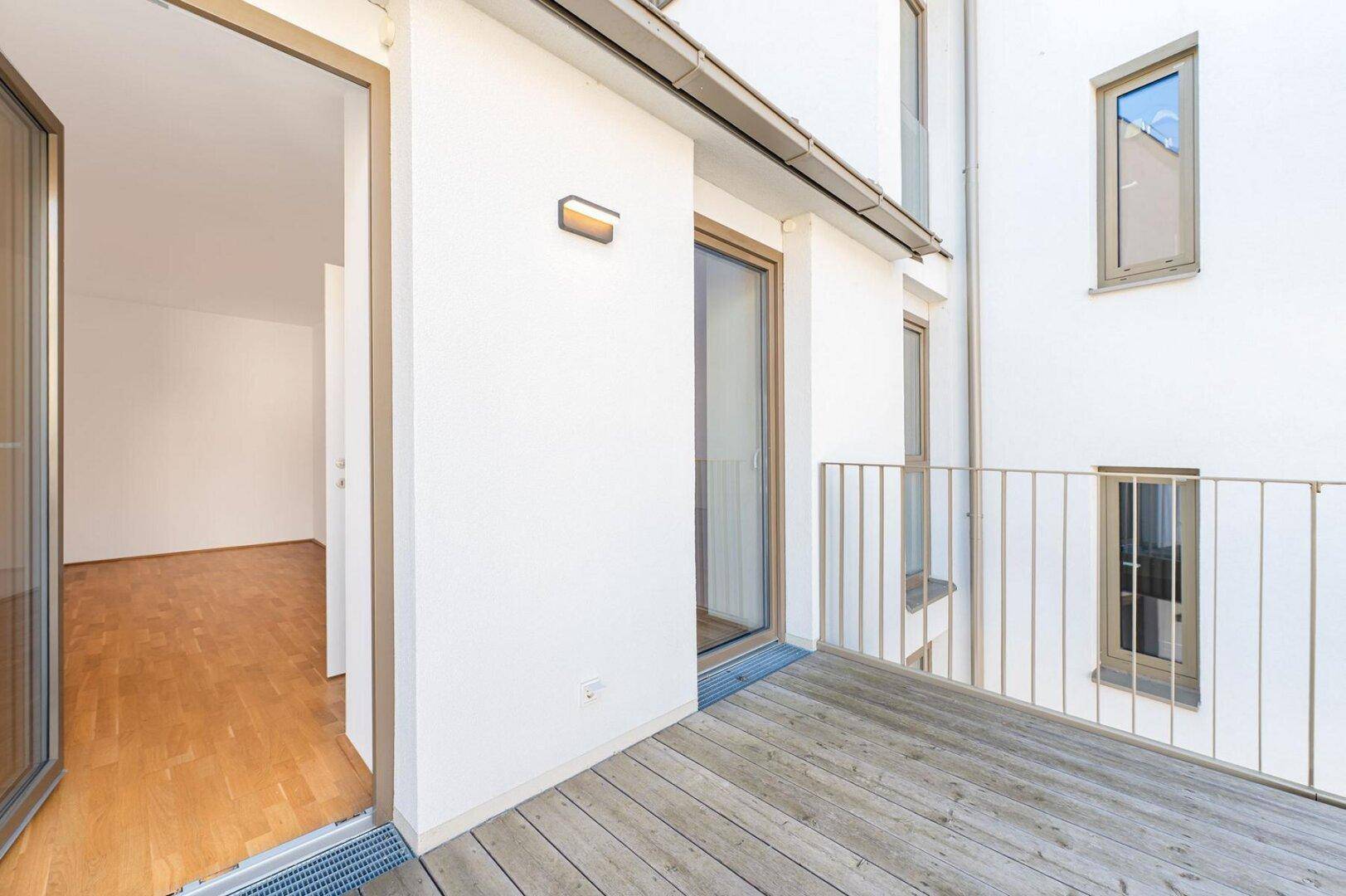 Moderner Balkon mit Holzdielen und direktem Zugang zu einem hellen Wohnbereich.