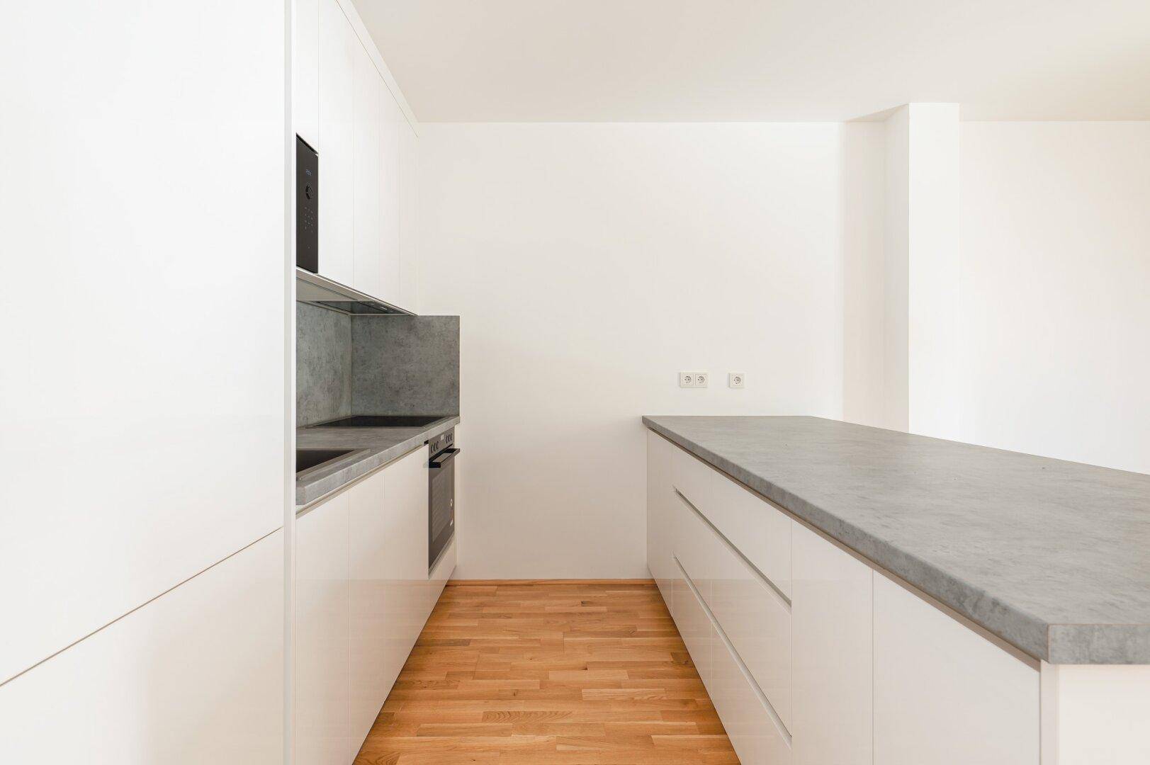 Moderne Einbauküche mit weißen Fronten, grauer Arbeitsplatte und integrierten Geräten.