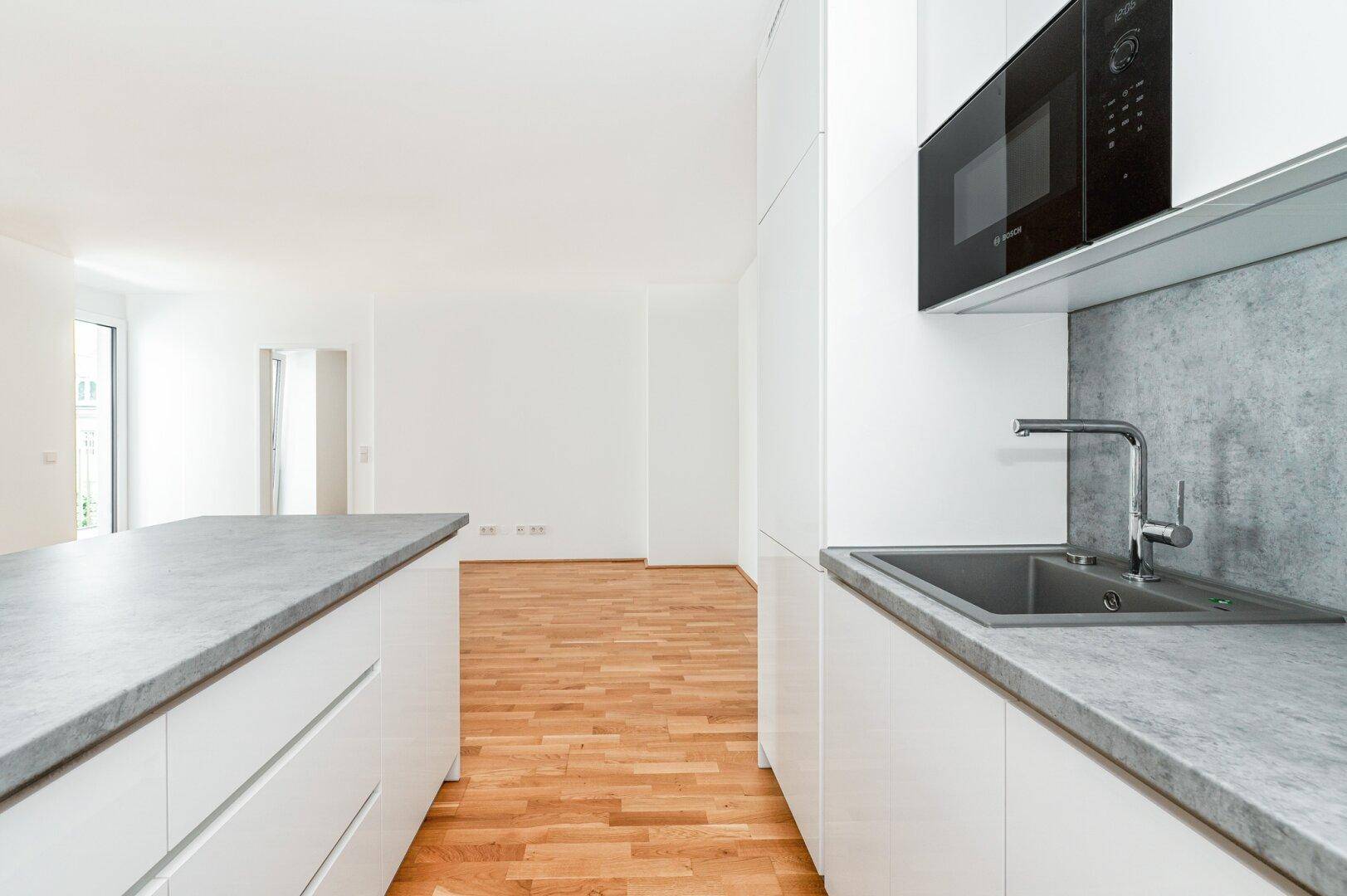 Helle Küche mit Spüle, integrierter Mikrowelle und moderner grauer Arbeitsplatte.