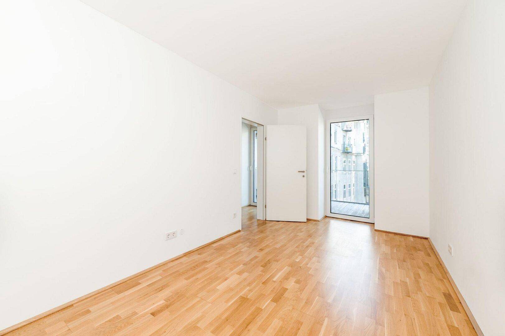 Helles Schlafzimmer mit Parkettboden und großen Fenstern, bereit zur individuellen Gestaltung.