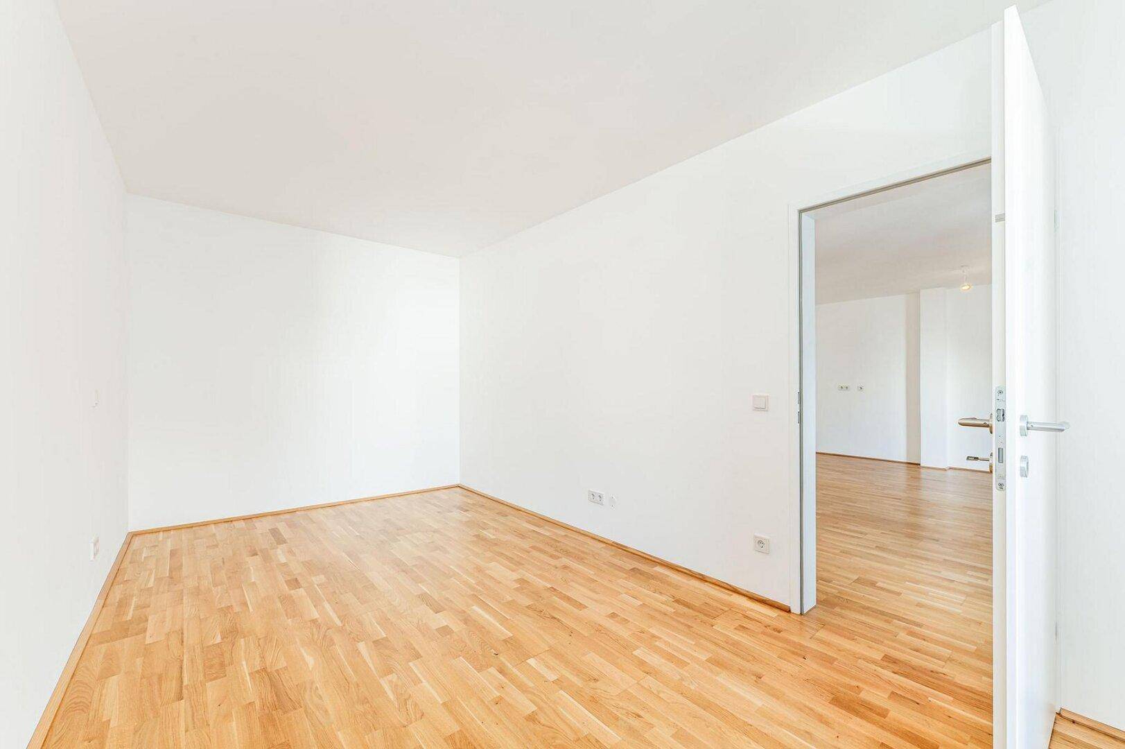 Leeres Zimmer mit Parkettboden und weiß gestrichenen Wänden, ideal als Schlaf- oder Arbeitszimmer.