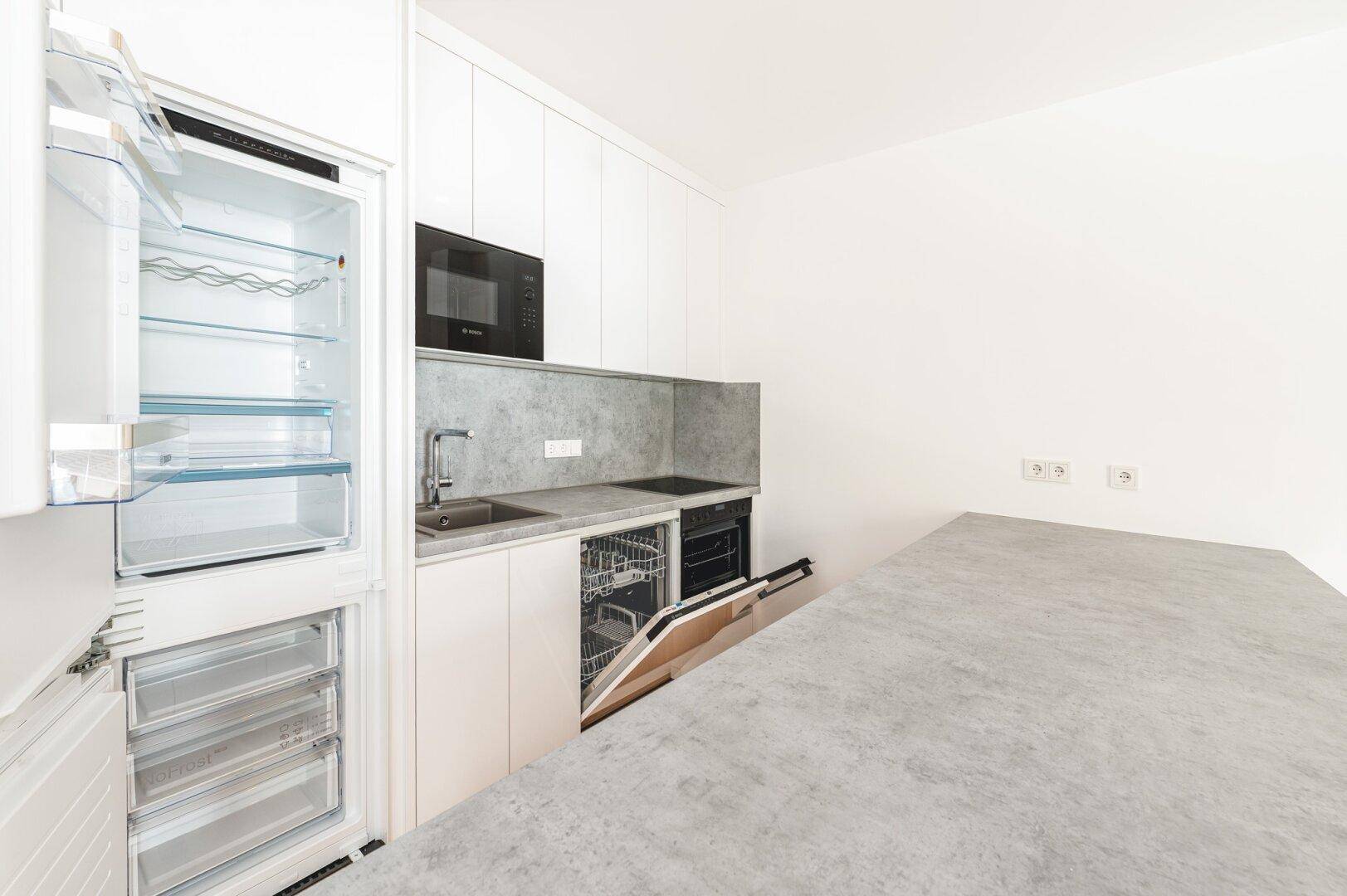 Voll ausgestattete Küche mit Kühlschrank, Geschirrspüler, Backofen und moderner Arbeitsplatte.