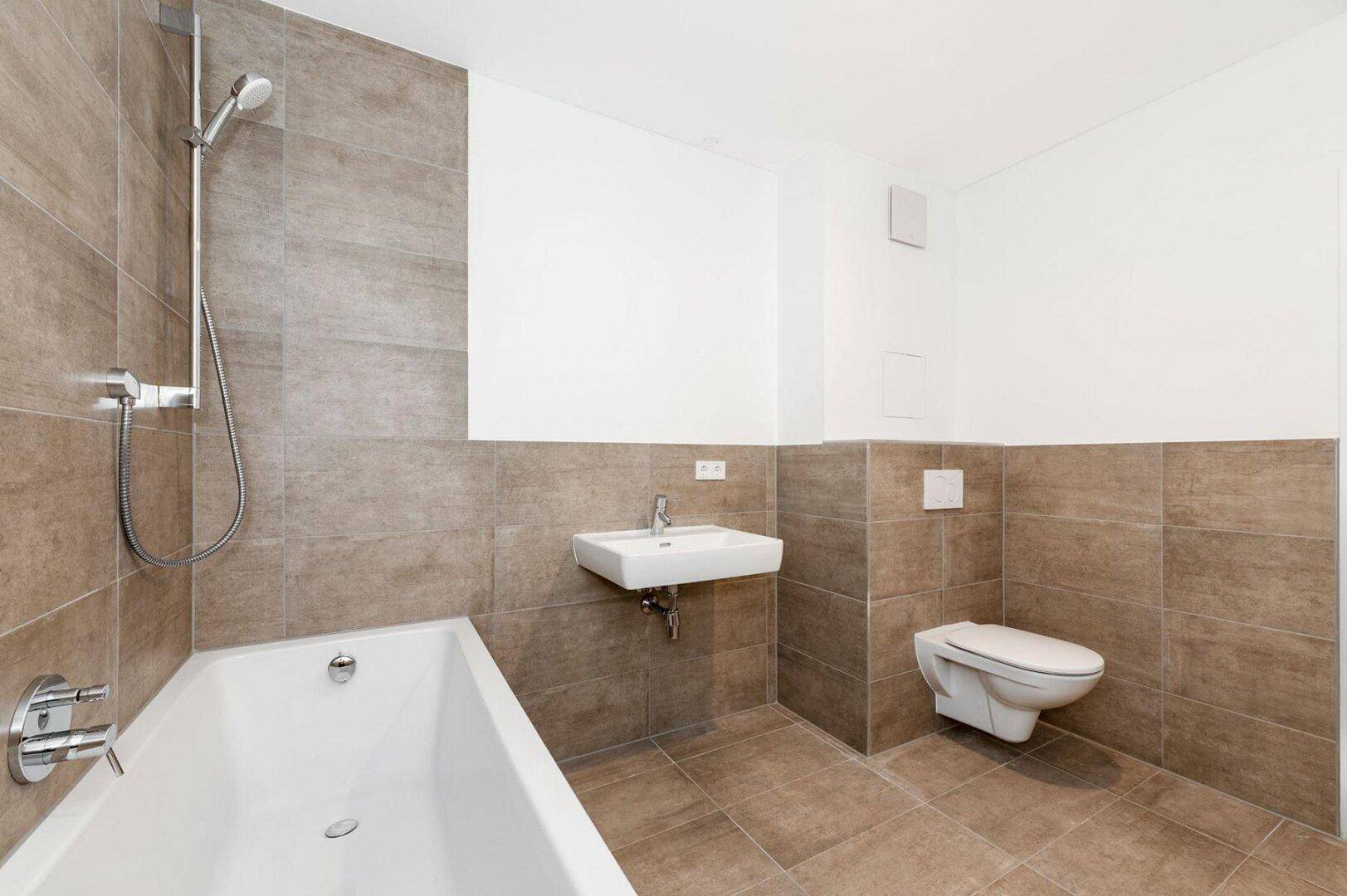 Helles Badezimmer mit Badewanne, WC und Einzelwaschbecken, komplett gefliest in Brauntönen.