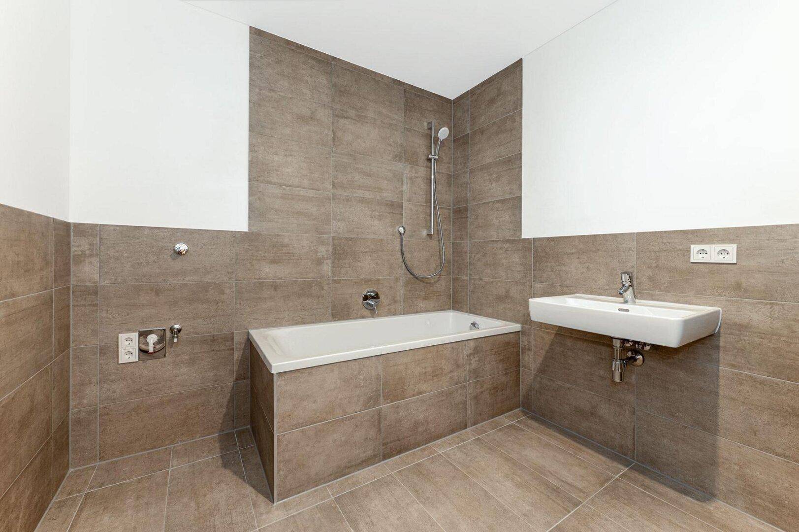 Modernes Badezimmer mit Badewanne, Einzelwaschbecken und braunen Fliesen an Wänden und Boden.