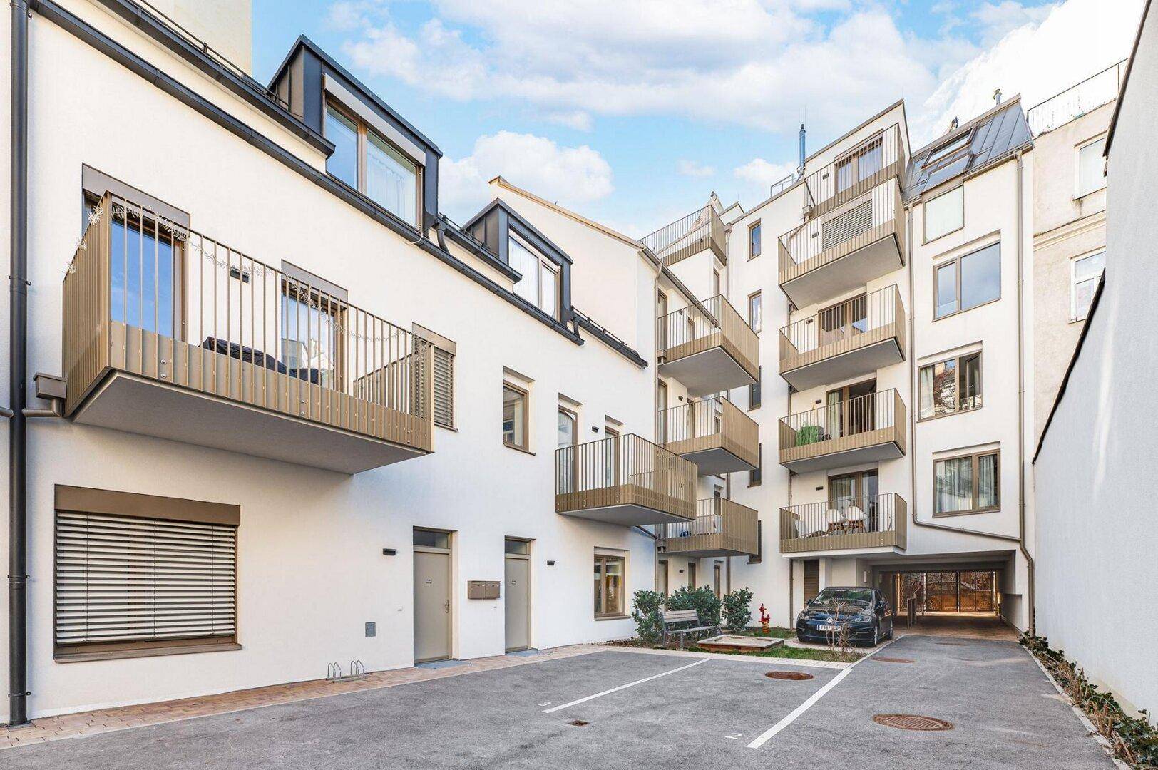 Moderne Gebäudefassade mit Balkonen und einem Innenhof mit Parkplätzen.