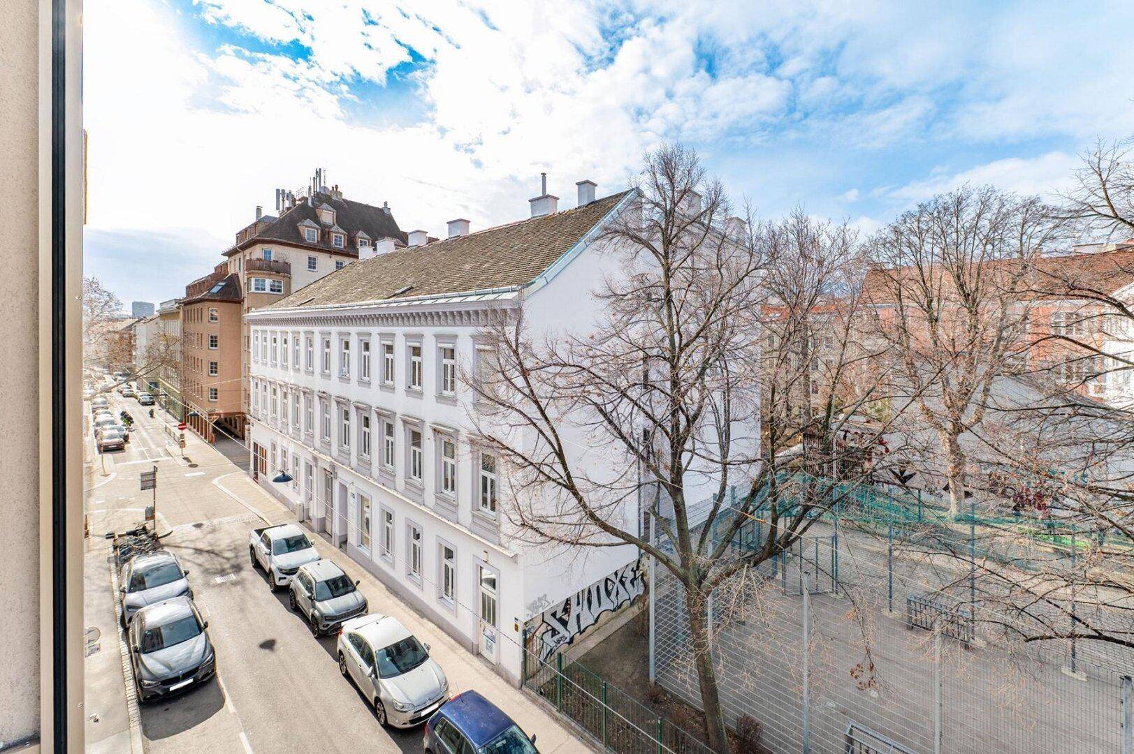 Weitläufiger Blick auf eine ruhige Stadtstraße mit parkenden Autos und Altbauten.
