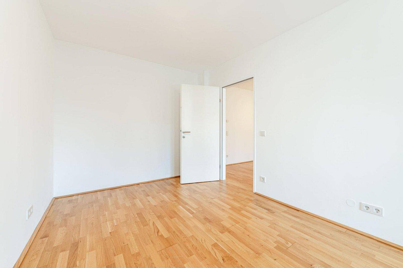 Leeres Zimmer mit hellem Parkettboden und weiß gestrichenen Wänden, bereit zum Einrichten.