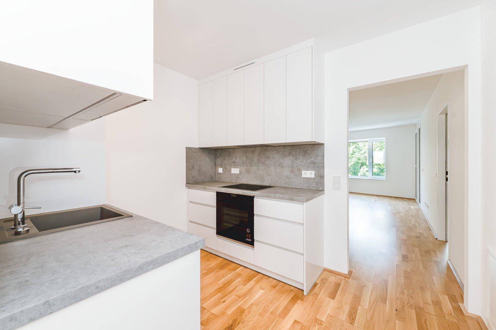Moderne Einbauküche mit weißen Schränken, grauer Arbeitsplatte und integriertem Backofen.