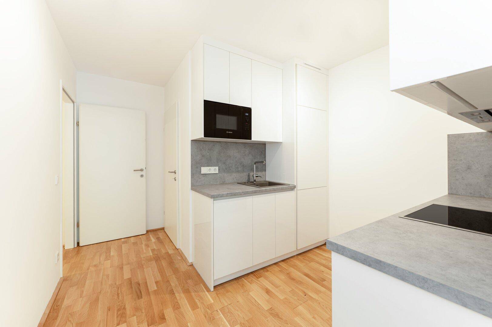 Kompakte Küche mit weißen Schränken, Mikrowelle und Spülbecken, ideal für kleine Wohnungen.