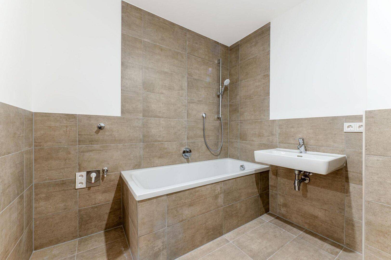 Modernes Badezimmer mit Badewanne, Waschbecken und braunen Fliesen an Wänden und Boden.