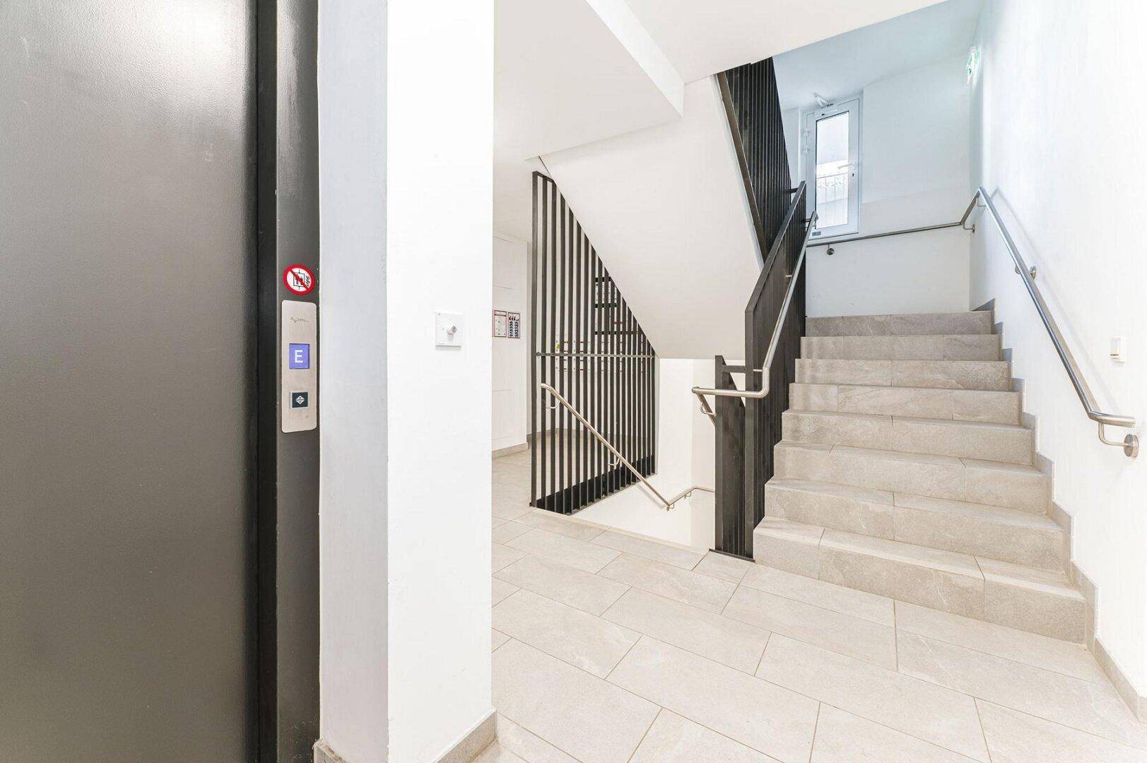 Modernes Treppenhaus mit Aufzug und Fliesenboden im Gemeinschaftsbereich des Gebäudes.