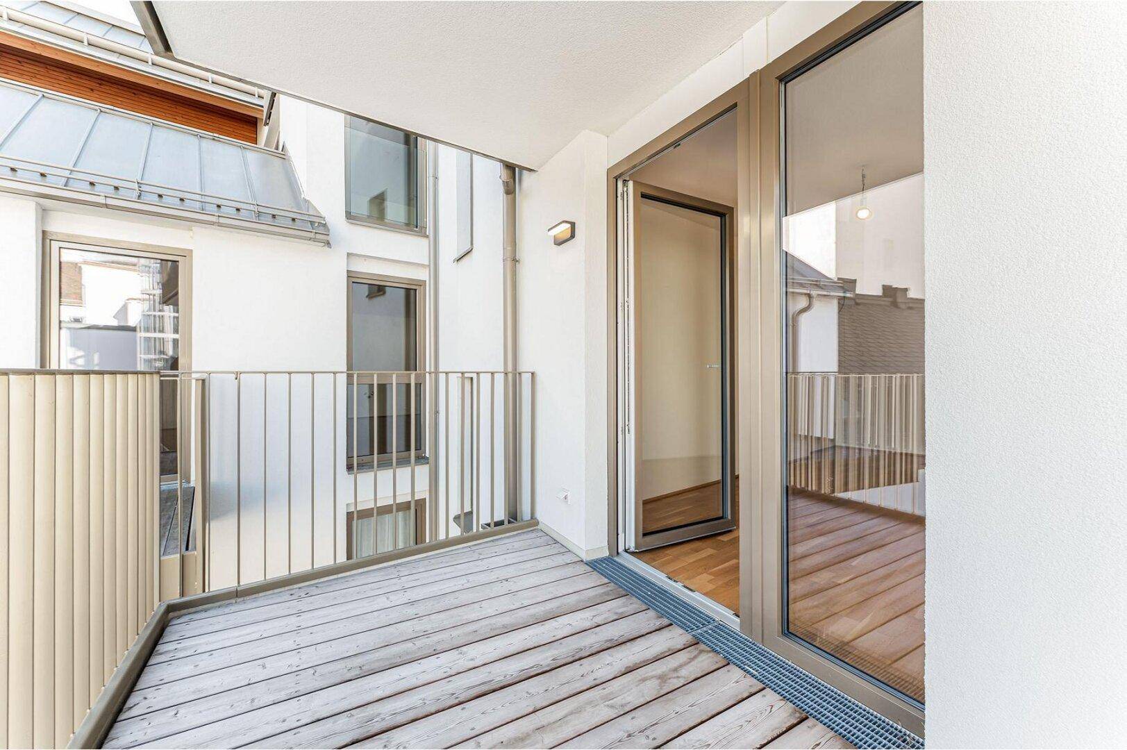 Balkon mit Holzboden und Zugangstür zum Innenraum, umgeben von der modernen Fassade des Gebäudes.