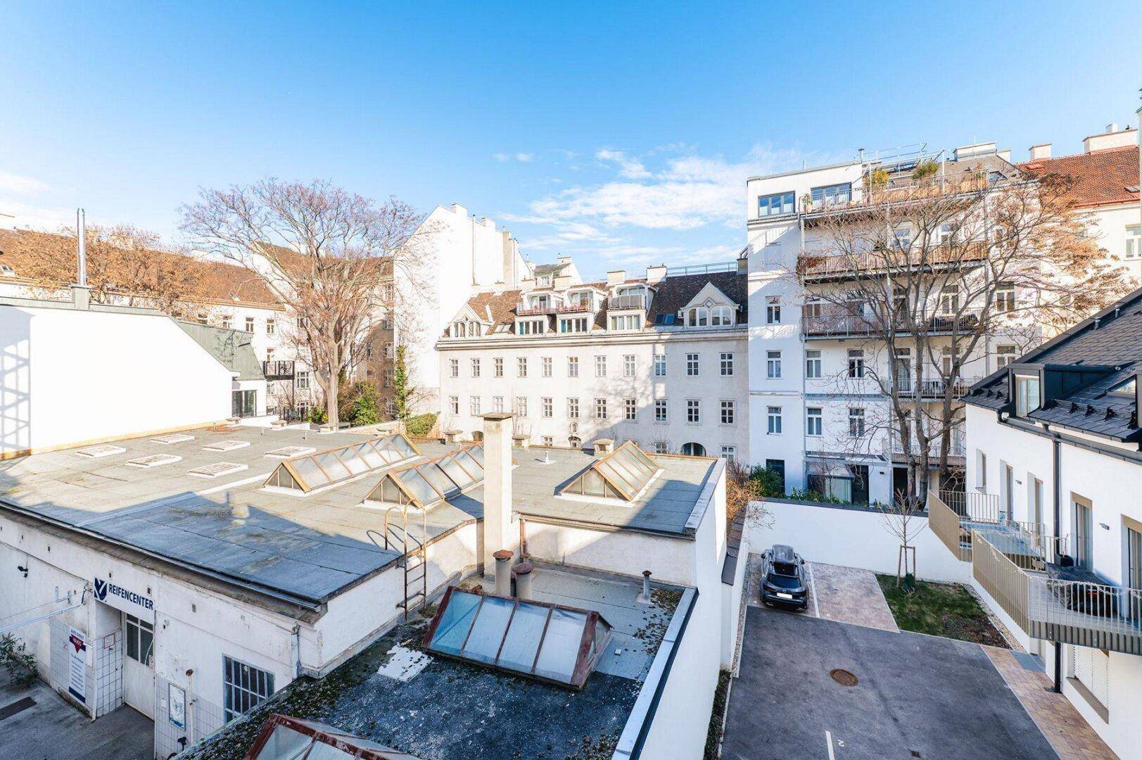Blick über die Dächer der umliegenden Gebäude, mit mehreren Dachfenstern und einem Innenhof mit Parkplätzen.