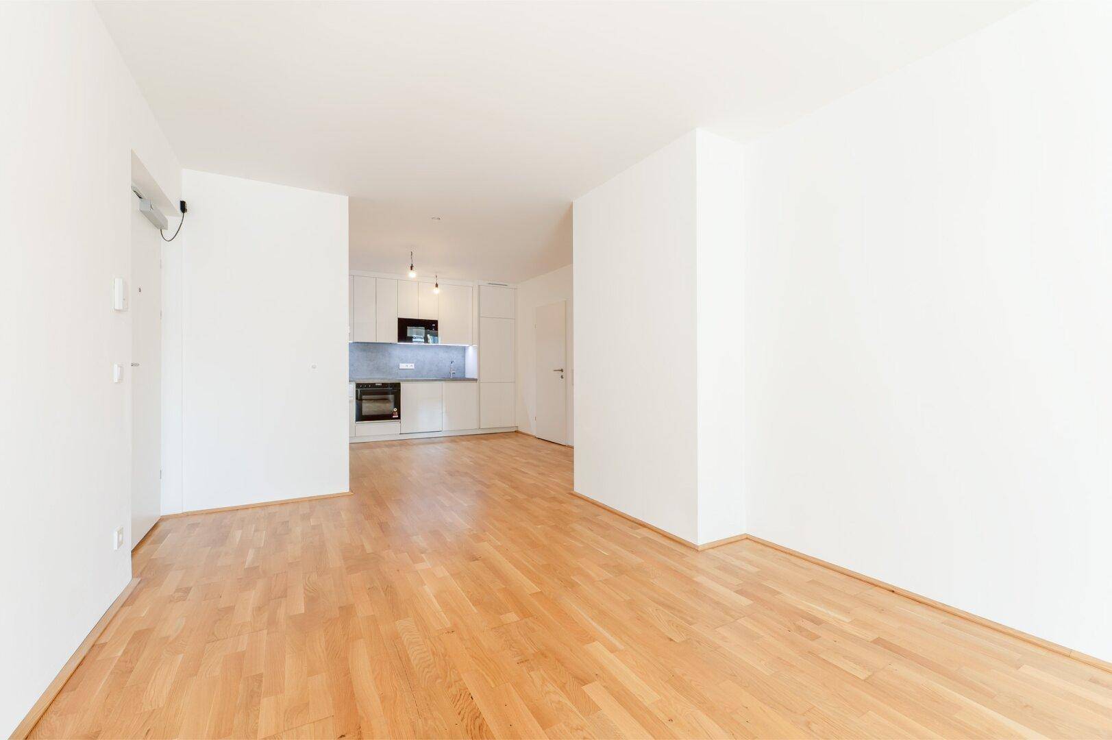 Offener Wohnbereich mit Parkettboden und Blick auf eine moderne, integrierte Küche mit weißen Fronten.