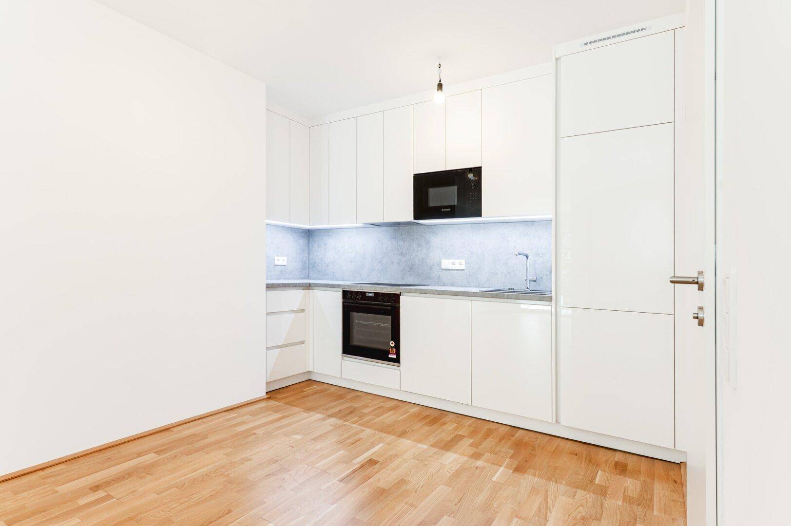Moderne Einbauküche mit weißen Hochglanzfronten, integriertem Backofen und Mikrowelle sowie Unterbauleuchten.