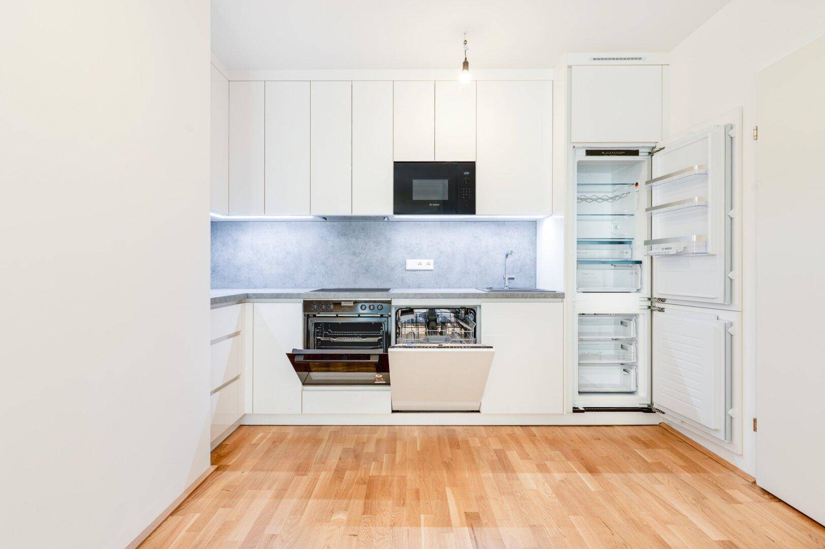 Voll ausgestattete Einbauküche mit geöffnetem Geschirrspüler und Kühlschrank, zeigt moderne Geräte.