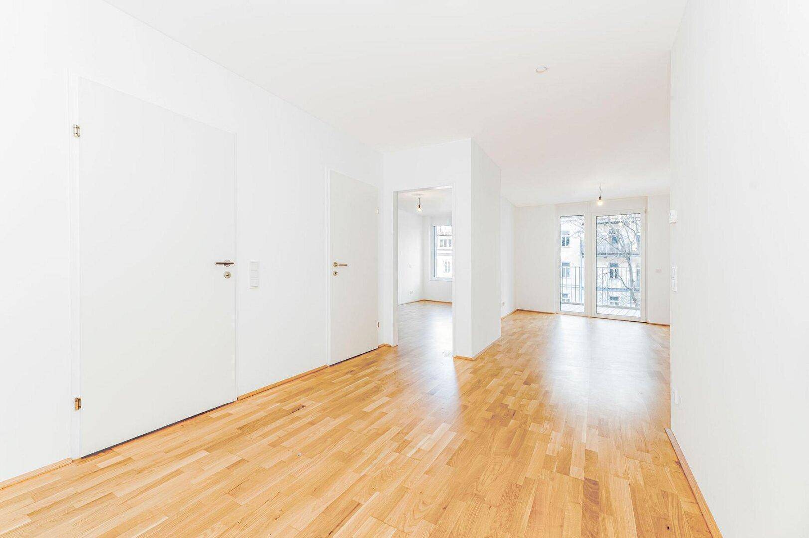 Heller Flur mit Parkettboden und weißen Türen, der zu verschiedenen Räumen und einem Balkon führt.