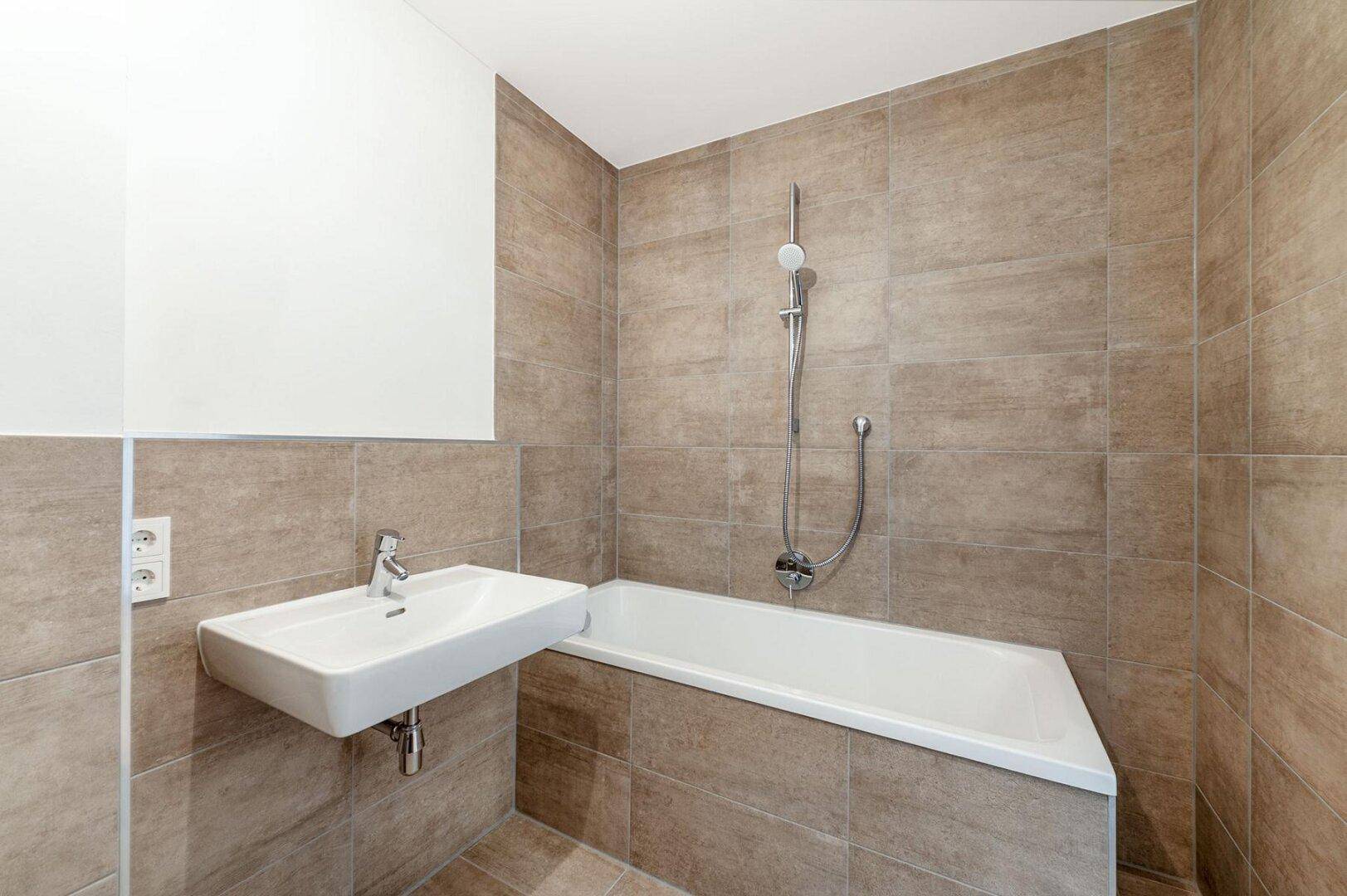 Modernes Badezimmer mit braunen Fliesen, einer Badewanne und einem einzelnen Waschbecken.