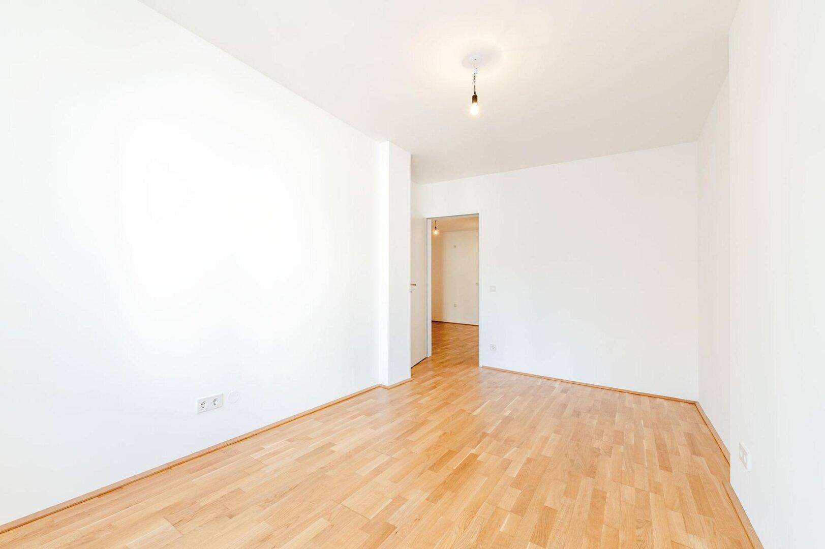 Ruhiges Schlafzimmer mit hellem Parkettboden und weißen Wänden, bietet eine neutrale Basis für individuelle Gestaltung.
