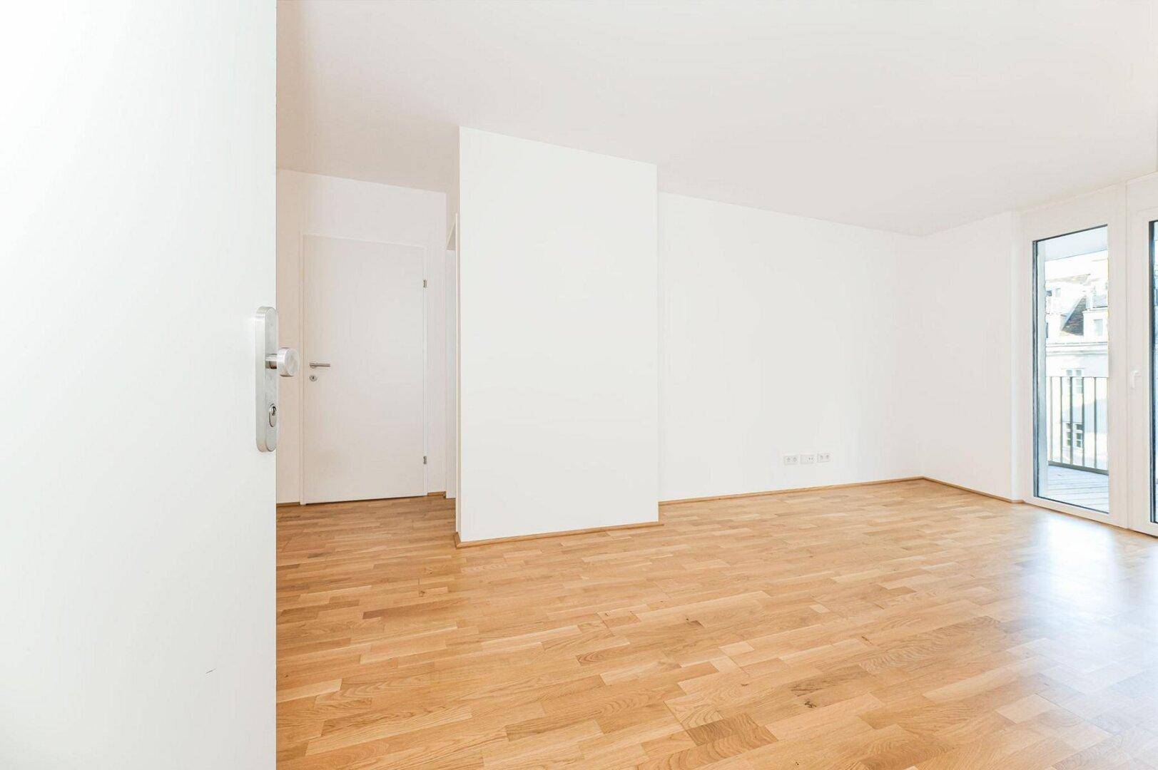 Geräumiger Wohnraum mit Parkettboden und Zugang zu einem Balkon, bietet viel Tageslicht.